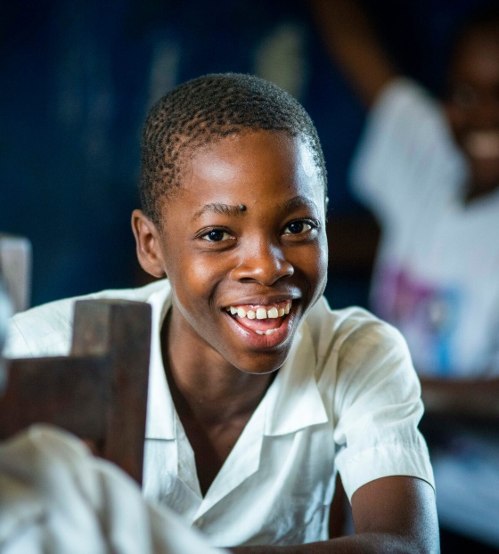 A boy sits in a classroom, smiling