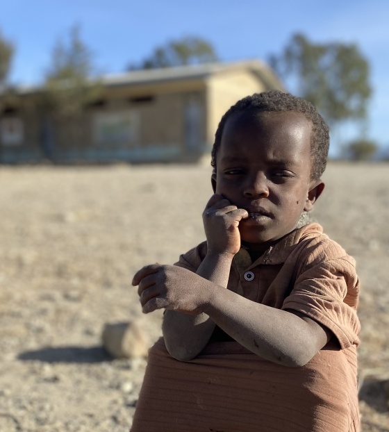 A child in Ethiopia sits on the dusty ground.