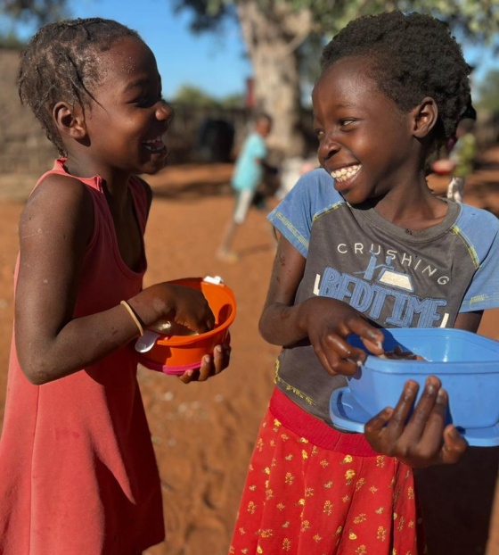 Happy children in Mozambique outside eating Mary's Meals