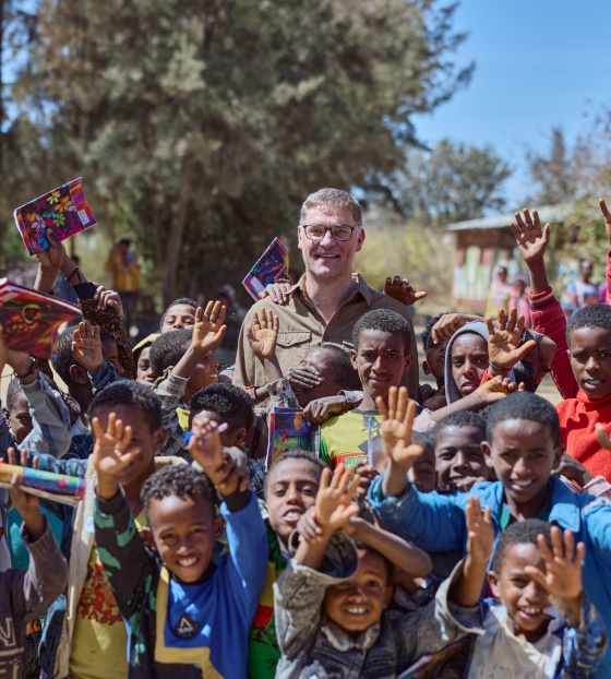 Magnus MacFarlane-Barrow standing alongside a group of happy school children in Ethiopia