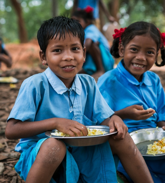 Two children sit together eating Mary's Meals