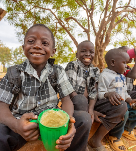 Boys in Zambia sit outside with mugs of Mary's Meals