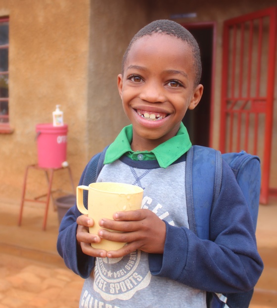 Image of a child holding their food outside of a school in Malawi