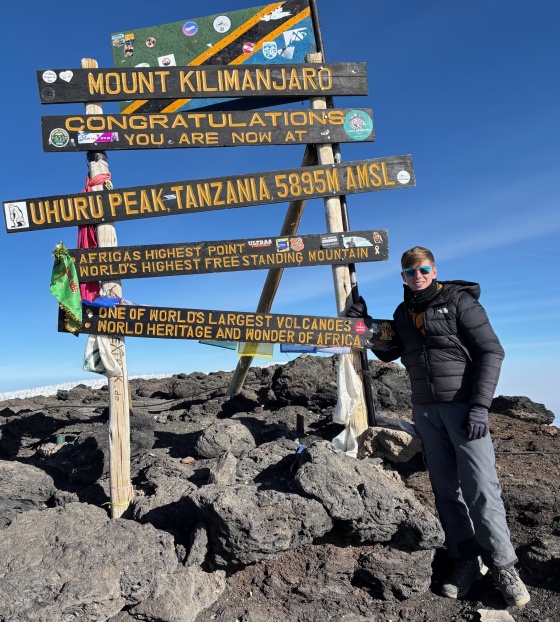 Teenager Lochlan stands at a sign signalling that he is at the summit of Mount Kililmanjaro