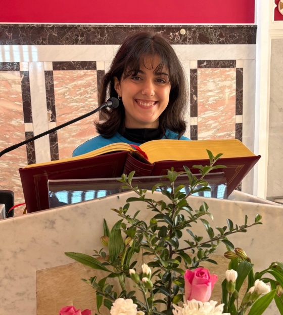 A woman, Alessandra, stands behind a pulpit in a church