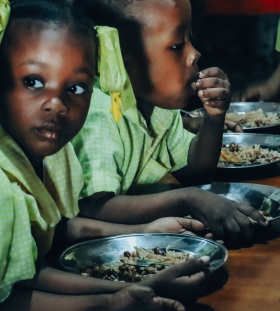 Children in Haiti eating meals at a long table
