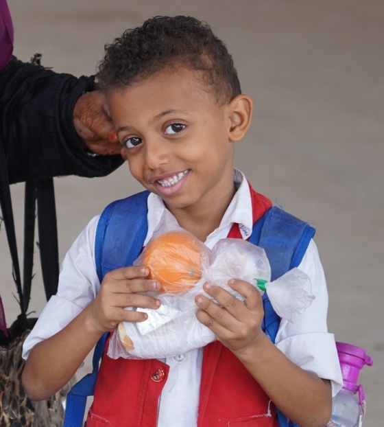 A young boy stands holding an orange