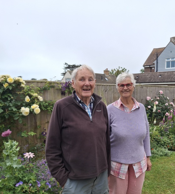 An elderly couple stand in a garden together