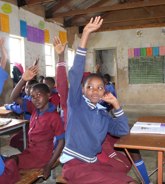 Kids in a classroom with their hands up