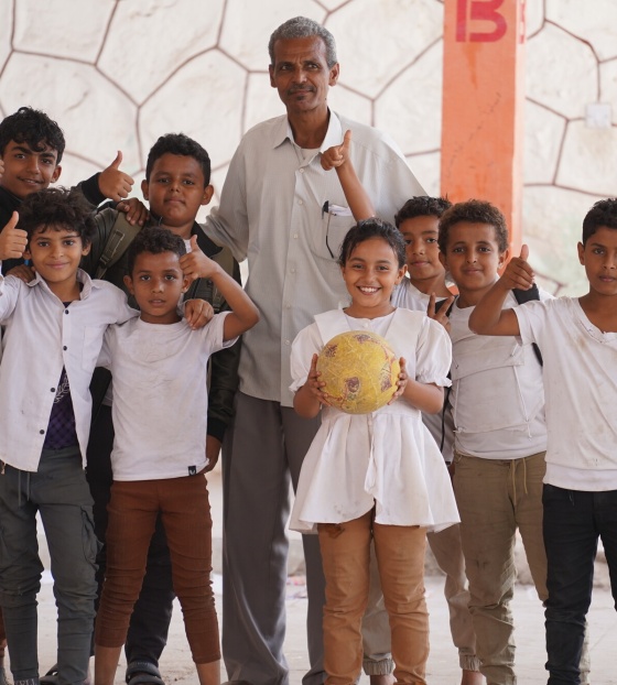 Mr Yasser, a member of school staff, stands with happy children