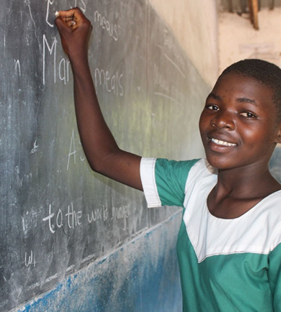 An image of a child in class writing on a chalkboard