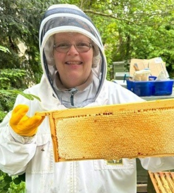 A woman in a beekeeping outfit holding honeycomb