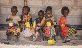 A line of children sitting against a wall eating