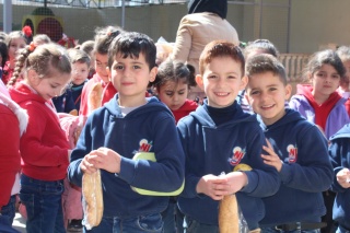 A group of young boys in Syria posing for a photo and each are holding baguettes