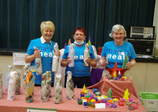 Three members of Blairgowrie volunteer group at a stall with crafts in Mary's Meals blue t-shirts