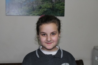 Small dark haired girl standing next to a wall smiling