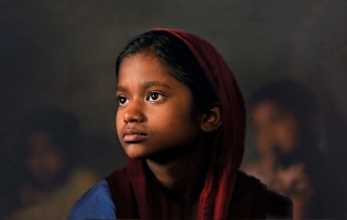 Child wearing red headscarf against a dark backdrop