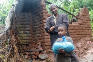 Child and person with bag of food in front of destroyed building, Malawi