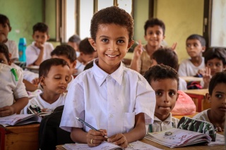 Smiling child in white shirt in foreground with class of children behind them