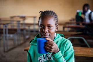 Schoolgirl holds blue mug while sitting in classroom