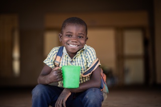 Smiling child holding mug of Mary's Meals porridge