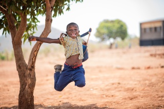 Boy jumps in celebration by a tree in Zambia
