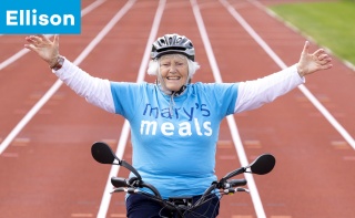 A woman sits on a trike on a running track with her hands in the air. The text reads 'Ellison'