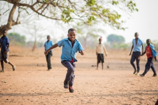 Boy running over sand near tree in Zambia with other children pictured in the background