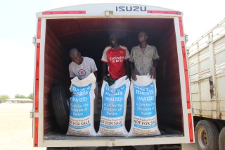 three men stand at the back of an open truck, holding bags of Mary's Meals maize to deliver to school