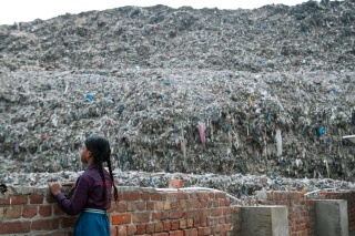 A girl looks over a wall to a large rubbish dump