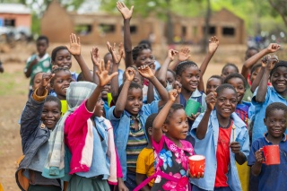 Children in playground at school in rural Zambia raise hands and smile