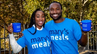 Scarlette and Stuart Douglas standing together smiling holding Mary's Meals mugs and wearing Mary's Meals t-shirts