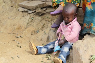 A child in Ethiopia sits on the dusty ground. Flies land on their face.