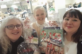 Grace, centre, stands with the fundraising Christmas packs she made for Mary's Meals. Two women stand either side of her.