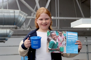 Lucy, a young fundraiser, stands holding a Mary's Meals mug and fundraising certificate