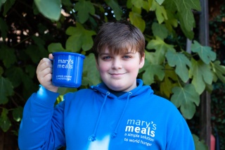 Michael, a young Mary's Meals supporter, stands in a Mary's Meals hoodie, holding a Mary's Meals mug