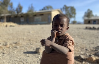 A child in Ethiopia sits on the dusty ground.