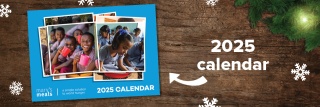 Mary's Meals 2025 Calendar sits on a festive wooden background with snowflakes and Christmas tree branches