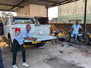 Mary's Meals delivery drivers in Malawi stand next to truck and motorbike