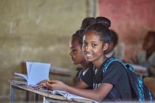 A teenager, Lydia, sits at a desk in a classroom