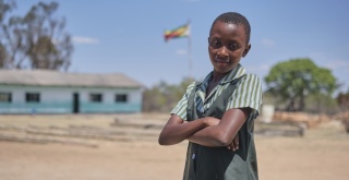 Kelcy a child from Zimbabwe looking to camera in a pinafore school uniform