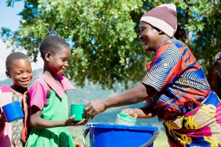 Image of volunteer cook giving school meal to child