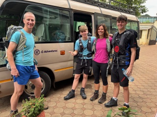 A family, mum, dad and two teenage sons, stand in hiking gear next to a mini bus