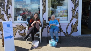 Beverley (right) and a fellow volunteer sit outside a shop knitting to raise money for Mary's Meals