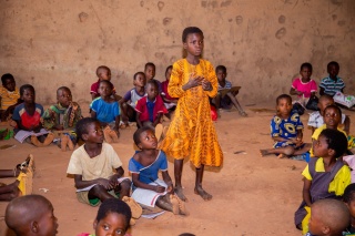 A child standing up and speaking in class while other children sit