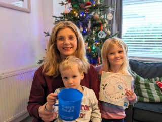 Victoria and her children in a living room, a boy holds a Mary's Meals mug and a girl holds a Santa plate