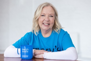 Deborah Meaden sitting smiling with her arms leaning on a table, next to a Mary's Meals mug