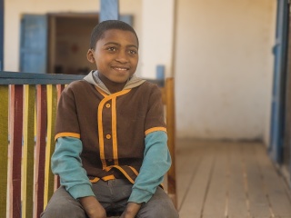 A boy, Mickael, sits smiling on a chair