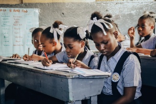 Children in Haiti sitting at a classroom desk writing