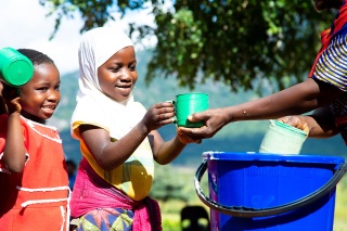 An image of a volunteer cook handing a school meal to a happy child